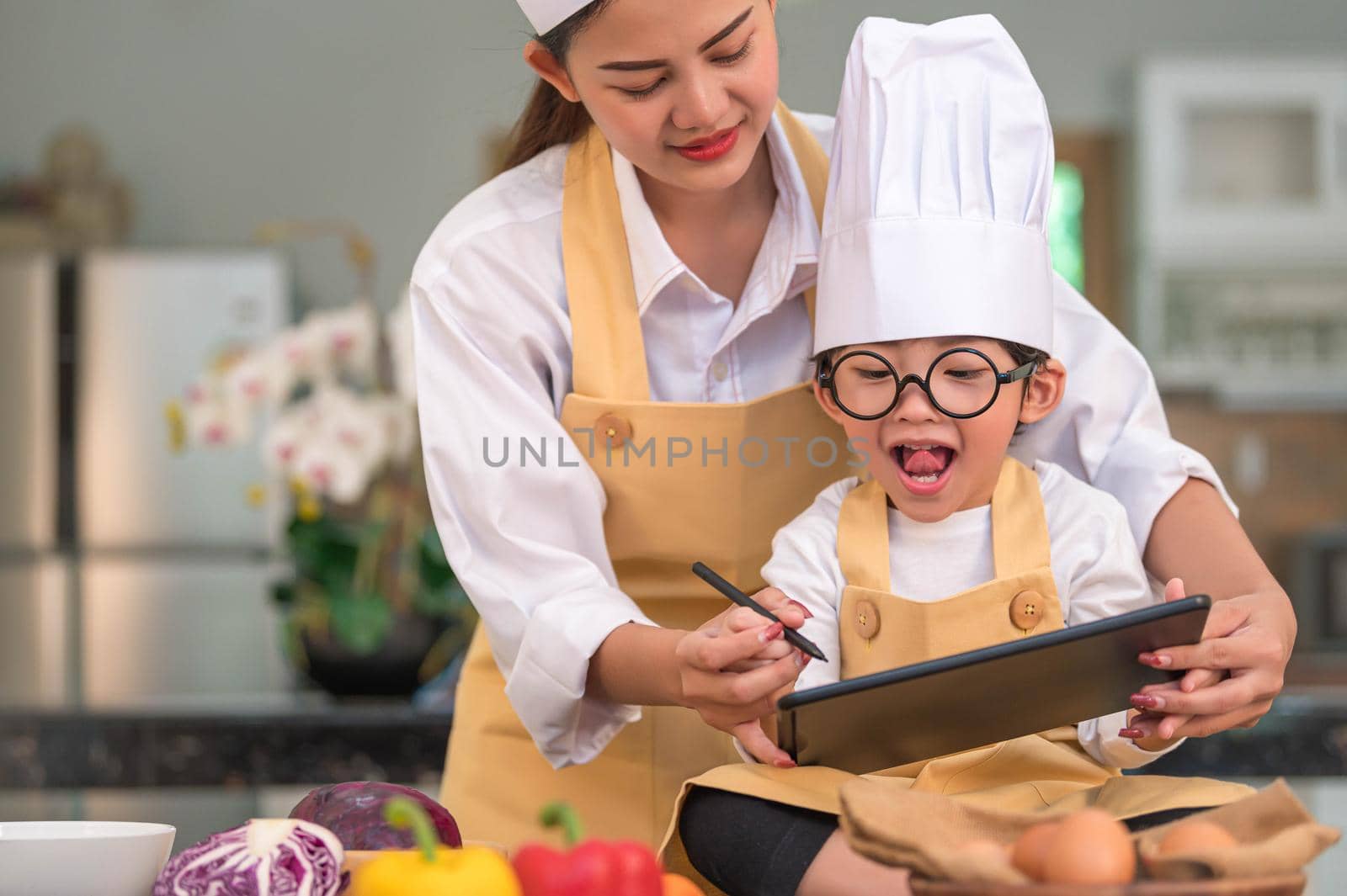 Beautiful Asian woman and cute little boy prepare online shopping and listing ingredient for cooking in kitchen at home with tablet. People lifestyles and Family. Homemade food and ingredient concept.