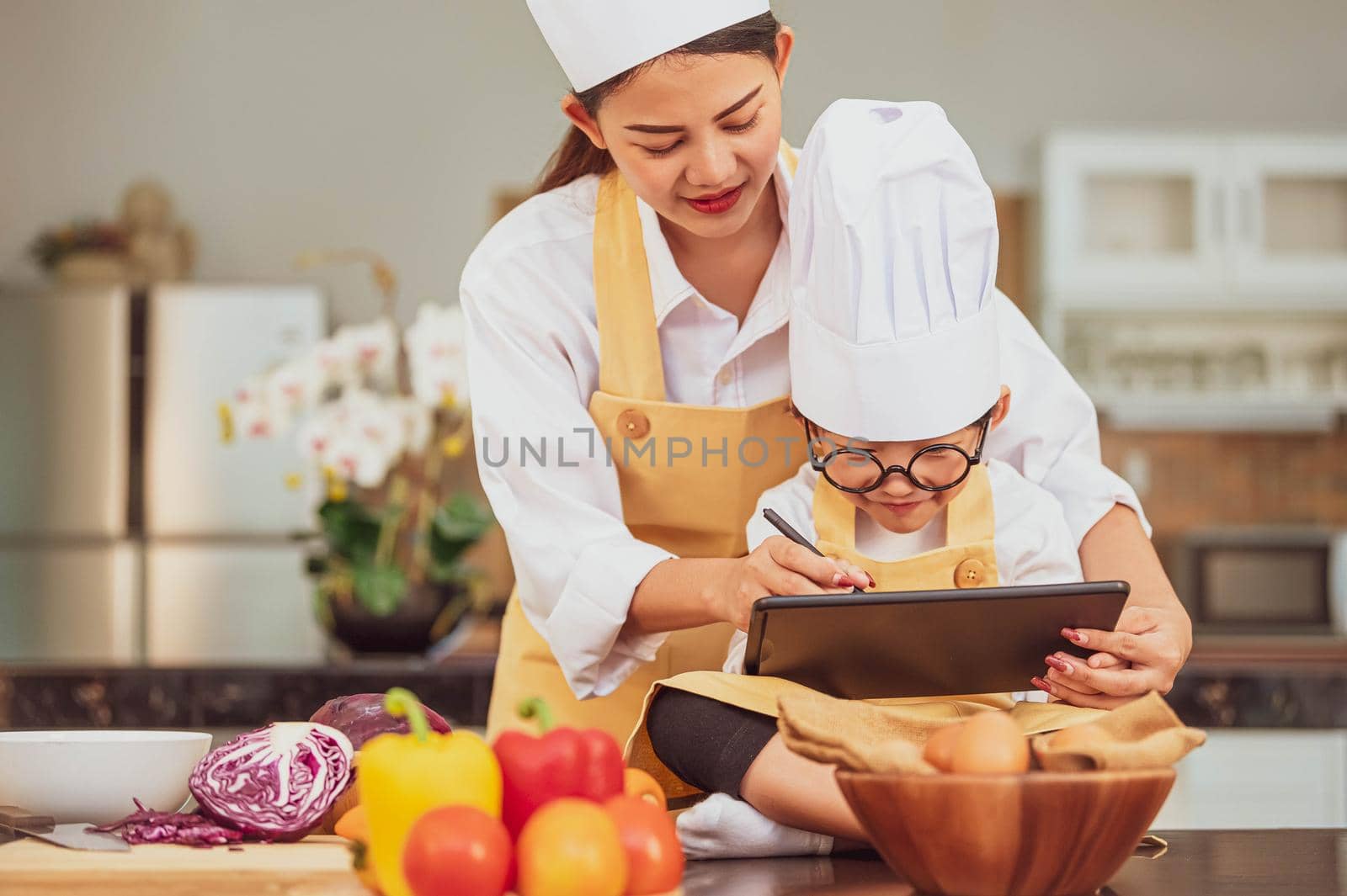 Beautiful Asian woman and cute little boy prepare online shopping and listing ingredient for cooking in kitchen at home with tablet. People lifestyles and Family. Homemade food and ingredient concept.