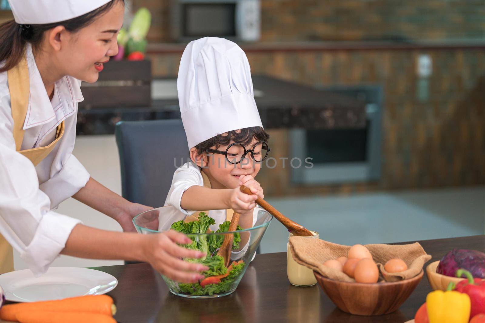 Happy beautiful Asian woman and cute little boy with eyeglasses prepare to cooking in kitchen at home. People lifestyles and Family. Homemade food and ingredients concept. Two Thai people life