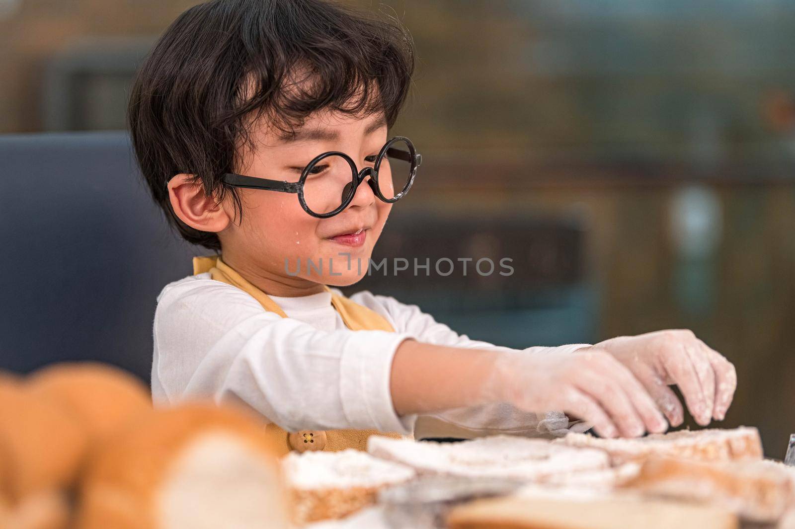 Portrait cute little Asian happiness boy interested in baking bakery with funny in home kitchen. People lifestyles and Family. Homemade food and ingredients concept. Baking Christmas cake and cookies