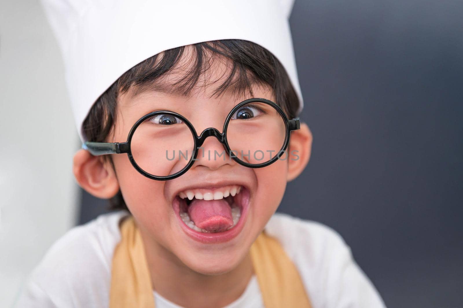 Portrait cute little Asian happy boy doing funny tongue face and interested in cooking in home kitchen. People lifestyles and Family. Homemade food ingredients concept. Baking Christmas cake and cook