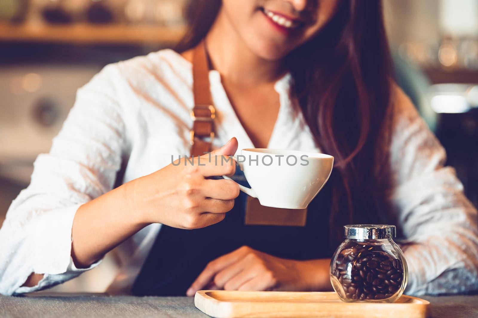 Closeup of professional female barista hand making and holding white cup of coffee. Happy young woman at counter bar in restaurant background. People lifestyles and Business occupation concept