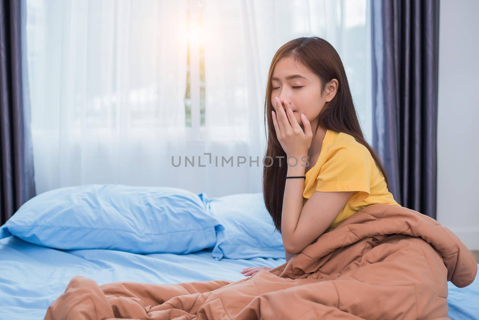 Asian woman getting up in morning in lazy posture in bedroom at home. People lifestyles and Health care concept. Overnight sleeping theme.