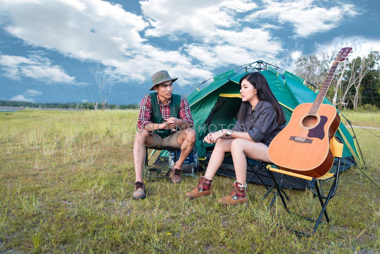 Two people talking near camping tent in meadow field. Male and female traveler looking at attraction view point. Couples adventure at outdoors together. People and lifestyles concept