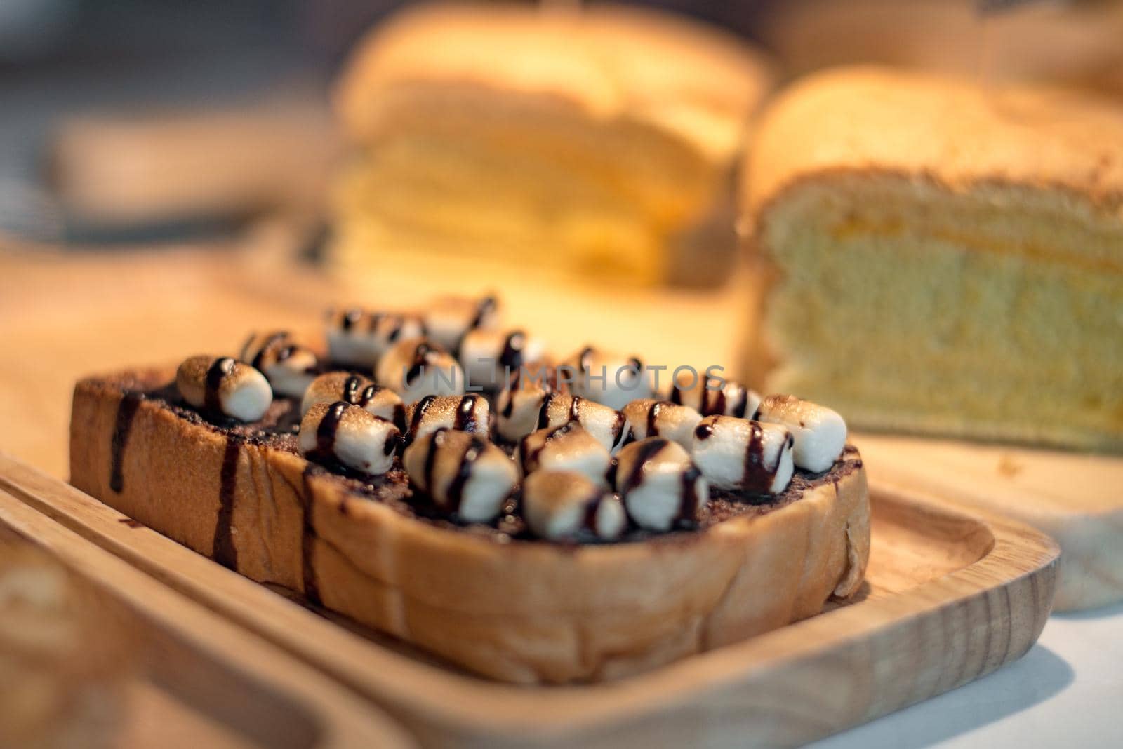 Sliced toasted bread with marshmello topping with chocolate sauce on wooden plate. Food and drinks concept. Bakery and coffee shop theme.