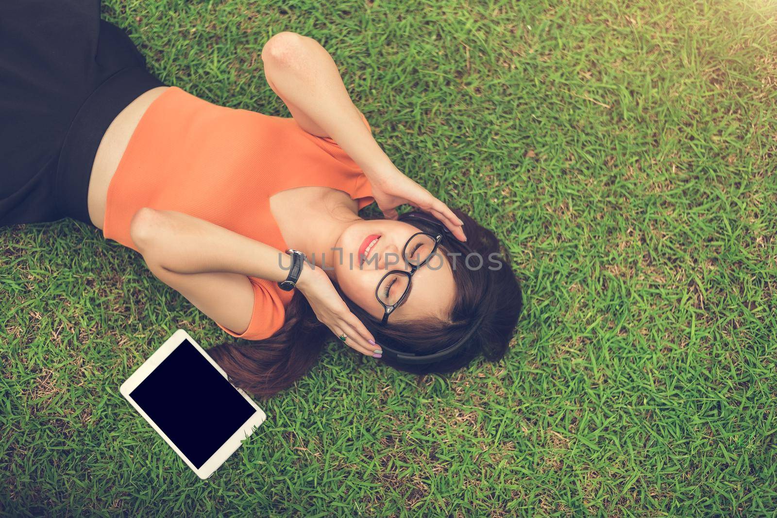 Asian woman listening music with blank tablet black isolated screen on grass in park. People lifestyle and entertainment concept.