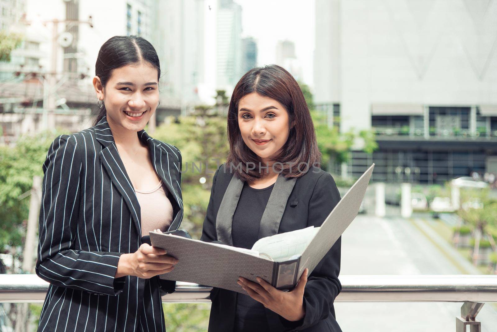 Two young Asian businesswomen looking into document file folder for analyzing profit or sale break even point after marketing. Business teamwork employees of lifestyle working women concept.