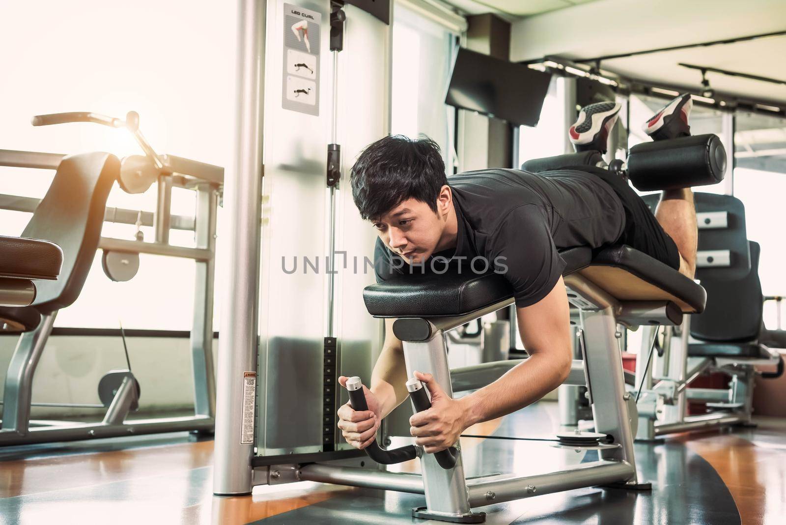 Asian sport man stretching and lifting weight by two legs when facing down for stretching muscle at fitness gym at condominium background. Sport and People lifestyles concept. Leg curl posture