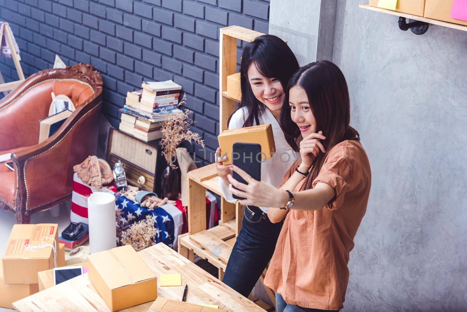 Two women took a selfie by mobile phone while selling online together. Business and people lifestyles concept. Thai girls take a photo while online shopping.