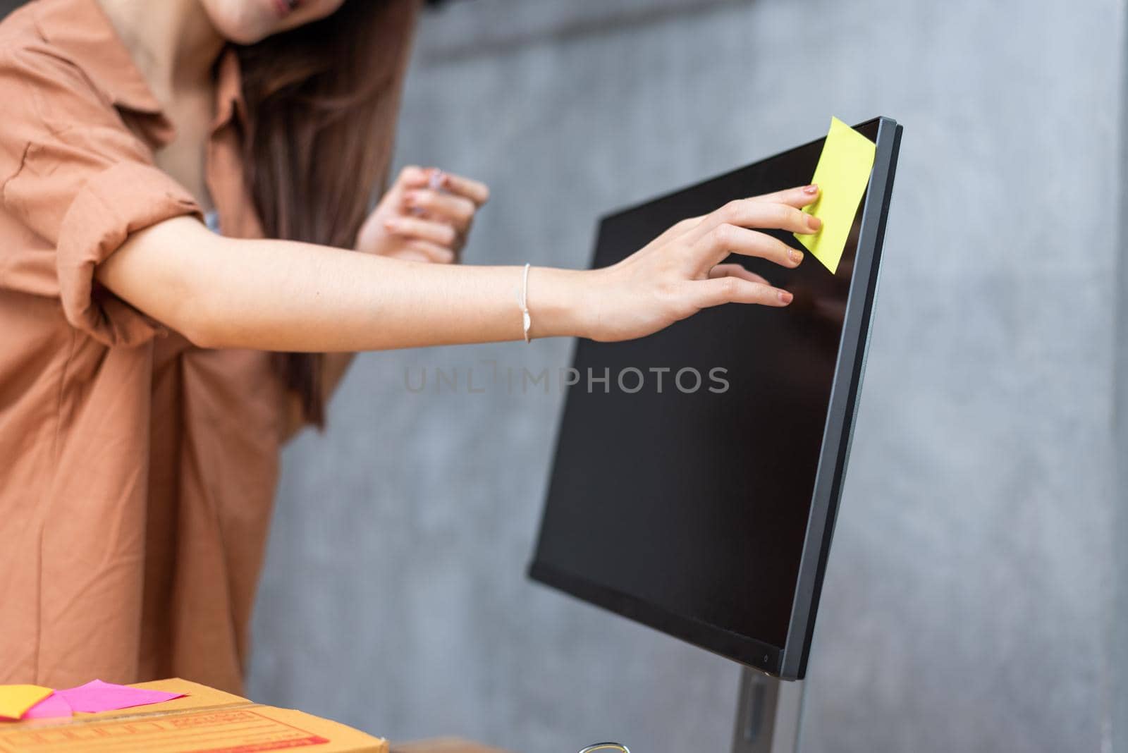 Business woman sticking order list memo on computer screen for reminding to send parcels to customers. Business and Service concept. Online shopping and Small business entrepreneur theme.