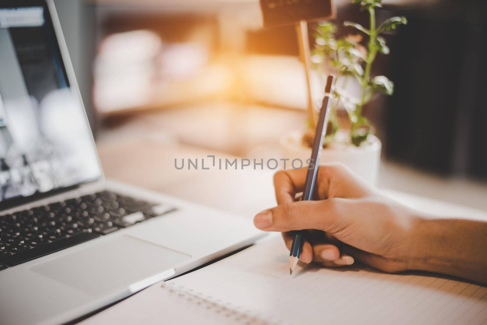 People hand using pencil to draw and noting on notepad. Laptop computer and small plant pot elements. Business and technology concept. Working in Cafe or coffee shop theme. Workaholic theme.