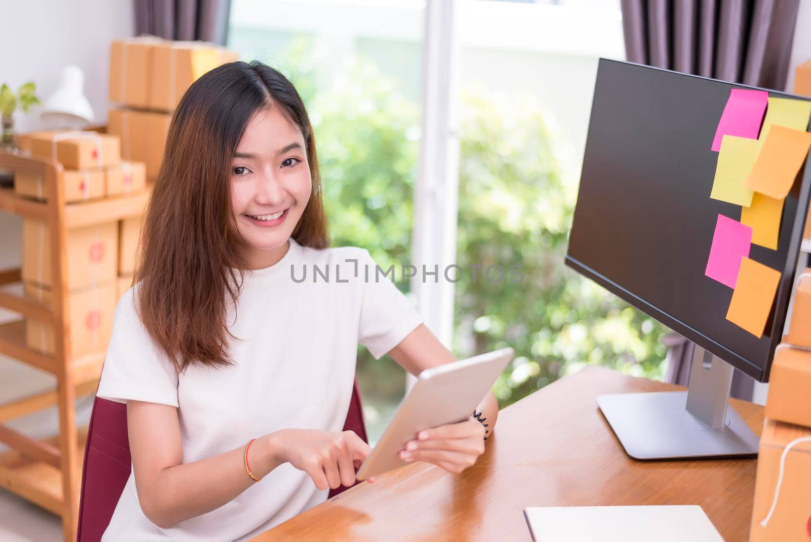 Asian woman using tablet with parcel boxes in delivery service theme. Part time and lifestyle concept