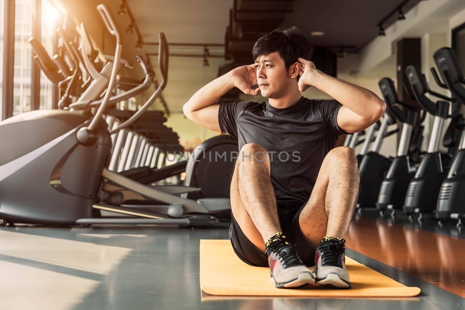 Sport man doing crunch or sit up posture on yoga mat in fitness gym at condominium with gym equipment background. Office working people lifestyles and Sport workout concept.