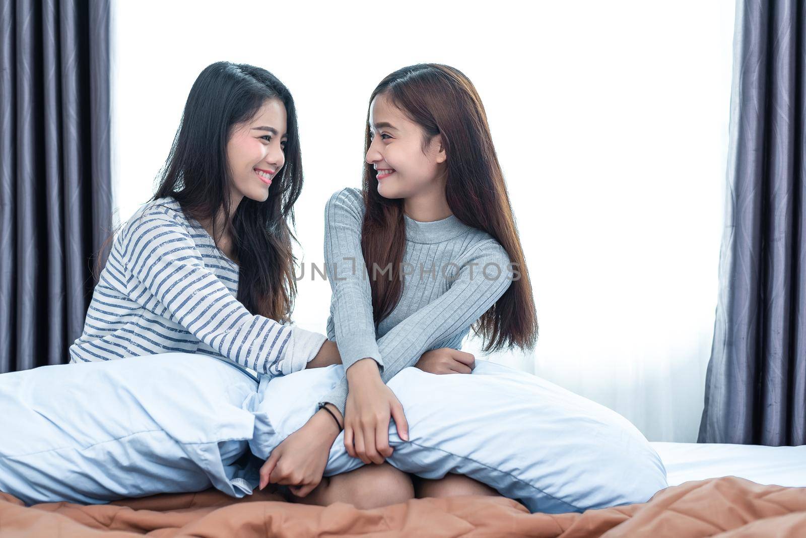 Two Asian Lesbian women in bedroom. Couple people and Beauty concept. Happy lifestyles and home sweet home theme. Cushion pillow element and window background.