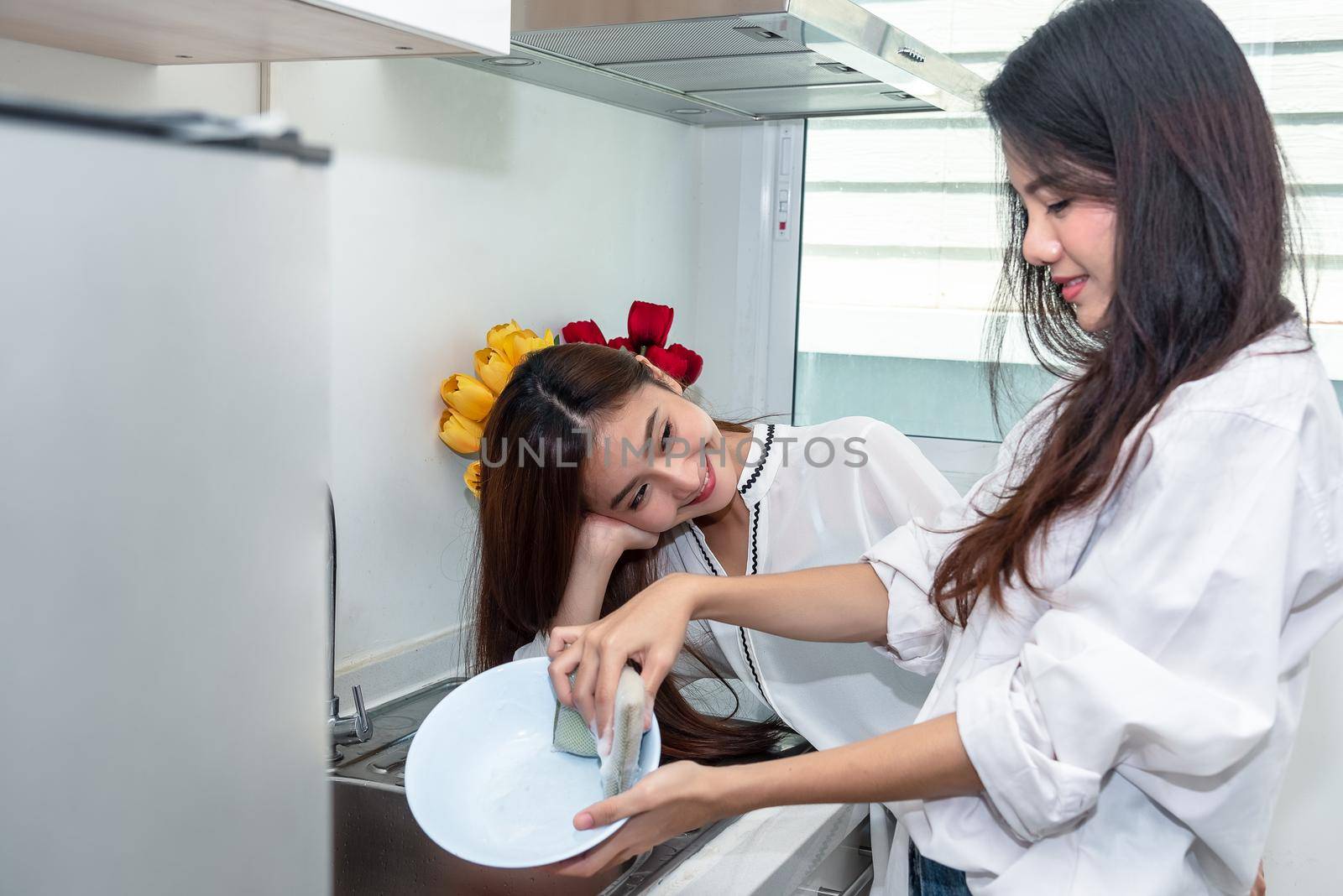 Two Asian women washing dishes together in kitchen. People and Lifestyles concept. LGBT pride and Lesbians theme.