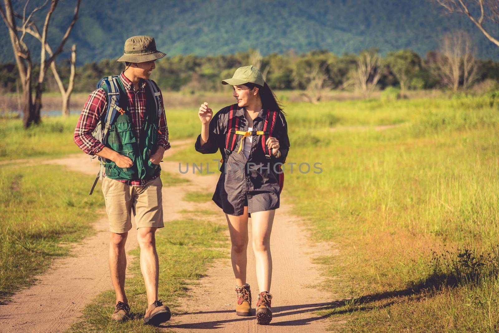 Two people walking on path in meadow field. Male and female traveler looking at attraction view point. Couples adventure at outdoors together. People and lifestyles concept. Trip and camping theme.