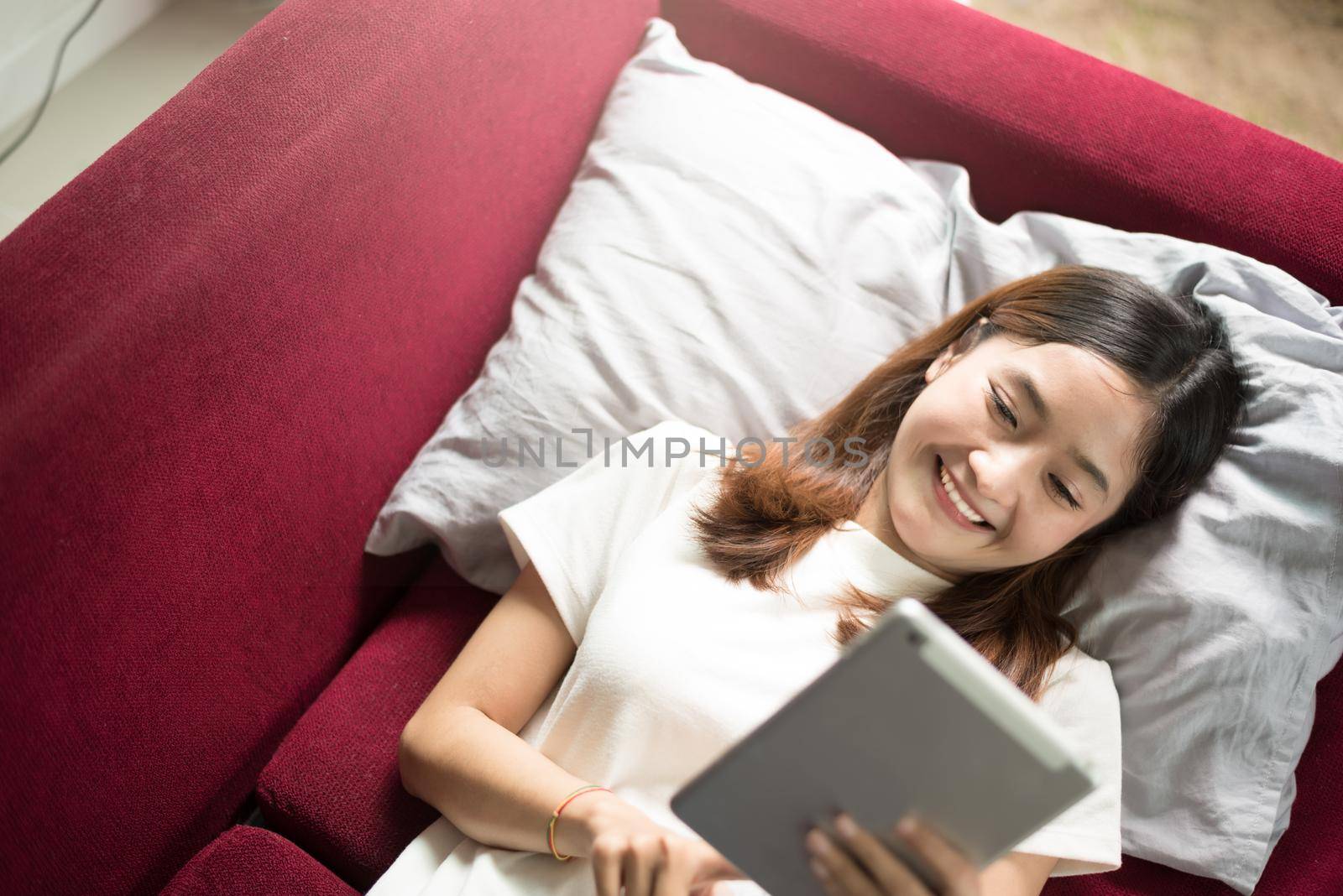 Woman enjoy relax at home with tablet on red sofa. Relax and Holiday concept