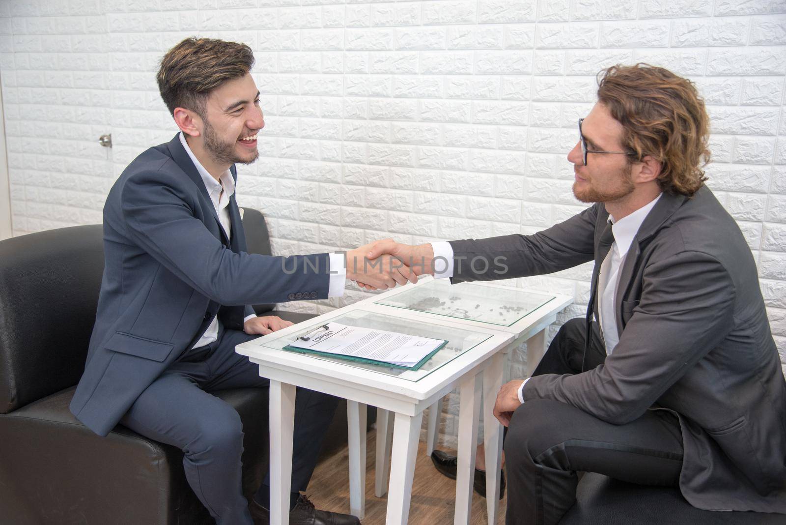 Two businessmen shake hand for contact and startup new project together on sofa indoors, Business and New project launch contact agreement concept