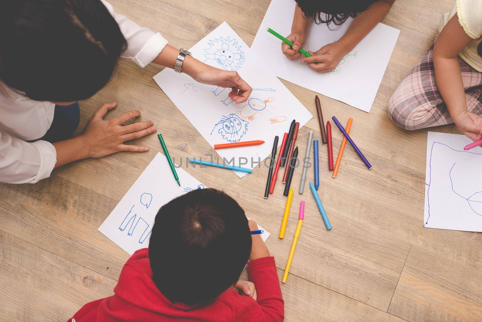 Asian mom teaching four little children to drawing cartoon in art class with color pen. Back to school and Education concept. Family and Home sweet home theme. Preschool kids theme. Top view angle