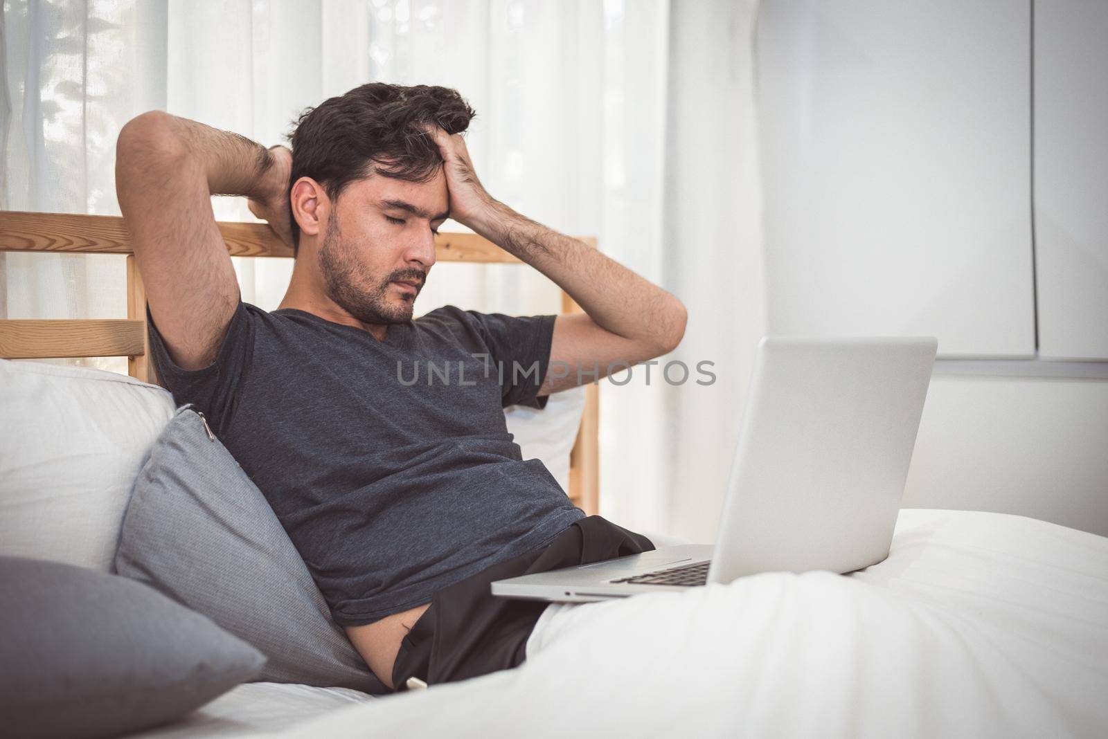 Man stressed out from work with laptop in bedroom. Technology and lifestyle concept. Social issues and problem. Healthcare and Office syndrome. Economic downturn and Critical deadline crisis theme.