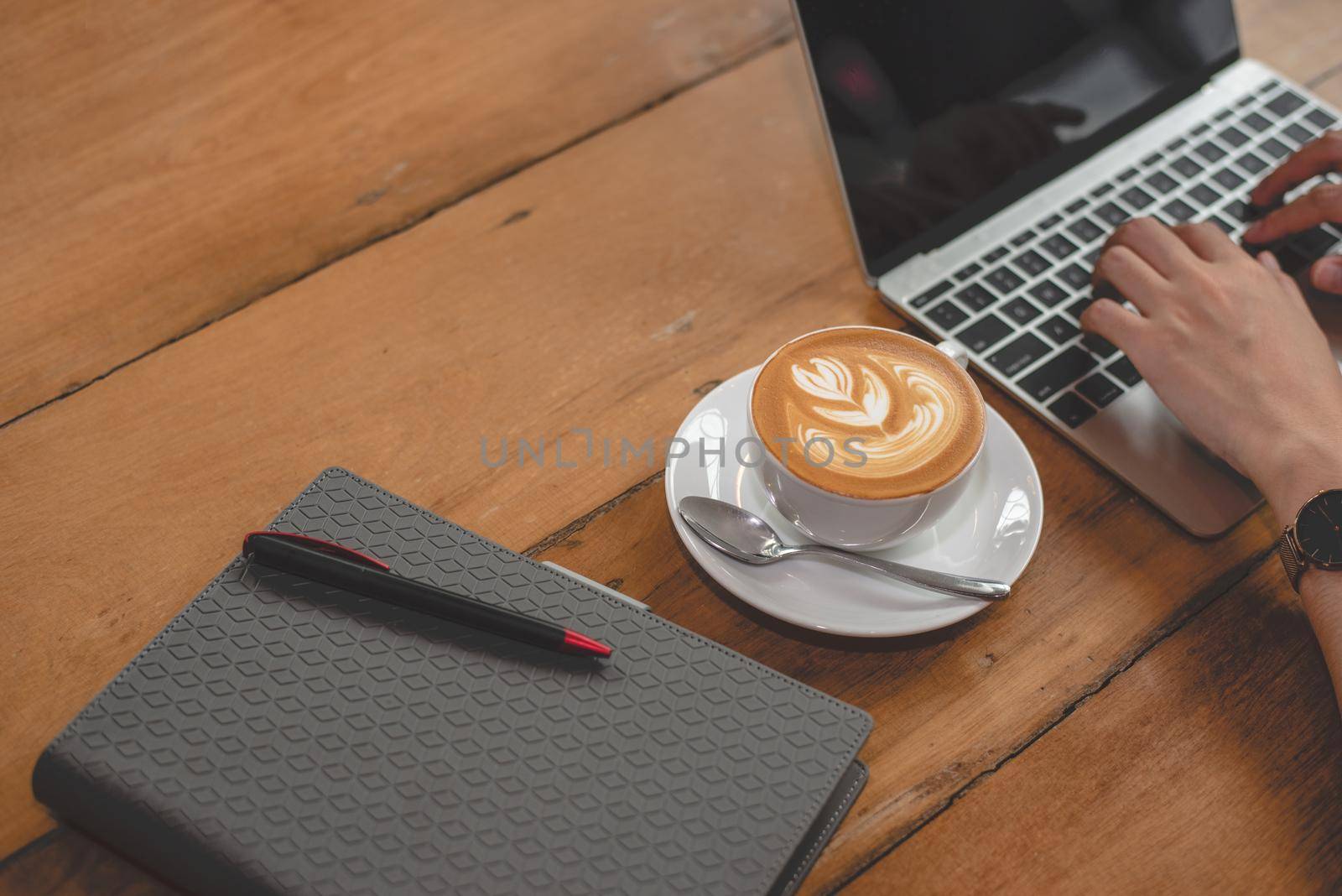 Close up of coffee cup with notebook and  woman hands using laptop. People and lifestyles concept. Freelance in coffee shop theme.