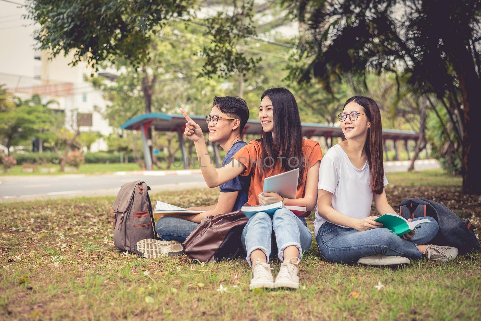 Group of Asian college student reading books and tutoring special class for exam on grass field at outdoors. Happiness and Education learning concept. Back to school concept. Teen and people theme. by MiniStocker