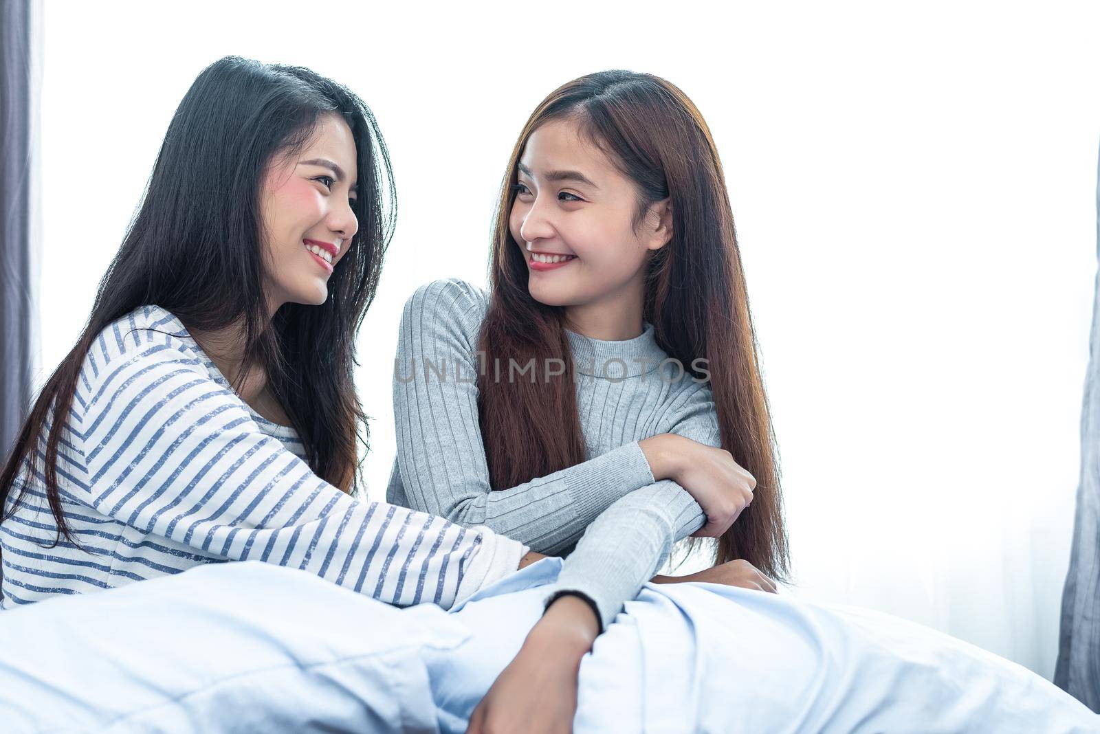 Two Asian Lesbian women looking together in bedroom. Couple people and Beauty concept. Happy lifestyles and home sweet home theme. Cushion pillow element and window background.