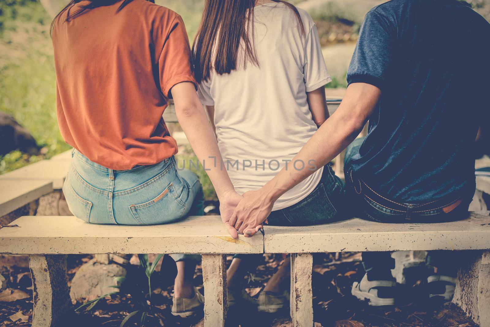 Boyfriend and another woman grab hands from behind together without sight of his girlfriend. Paramour and divorce concept. Social problem and cheating couples theme. Teen adult and University theme.