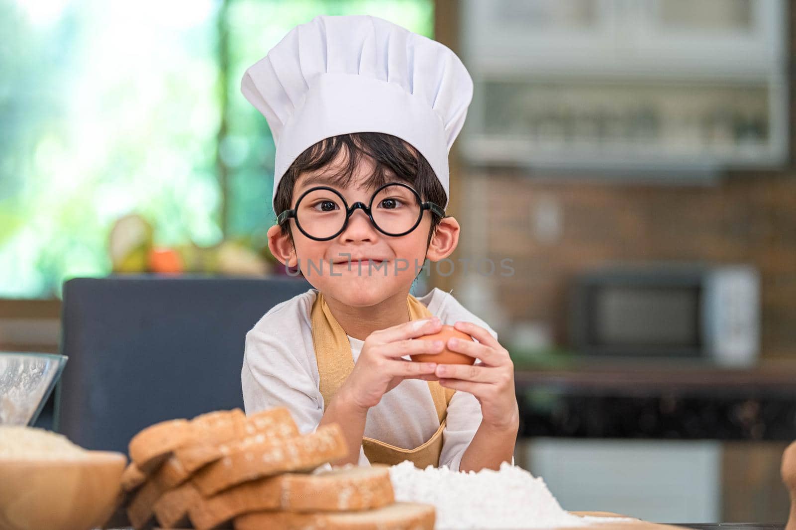 Portrait cute little Asian happy boy interested in cooking funny in home kitchen. People lifestyles and Family. Homemade food and ingredients concept. Baking Christmas cake and cookies. Smiling child