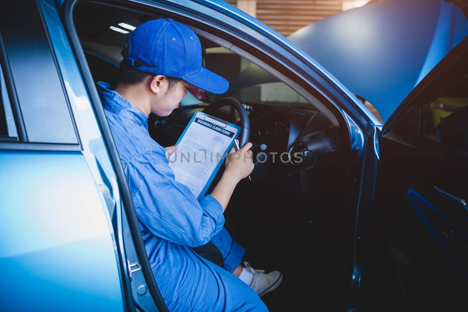 Mechanic holding clipboard and checking inside car to maintenance vehicle by customer claim order in auto repair shop garage. Repair service. People occupation and business job. Automobile technician