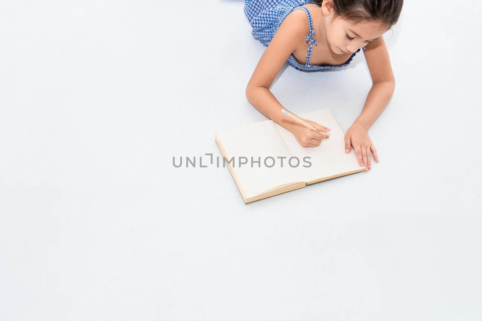 Top view of happiness girl drawing in sketch book on white floor at home or nursery. People lifestyle and kids play. Education and Children concept. Back to school theme. Copy space background