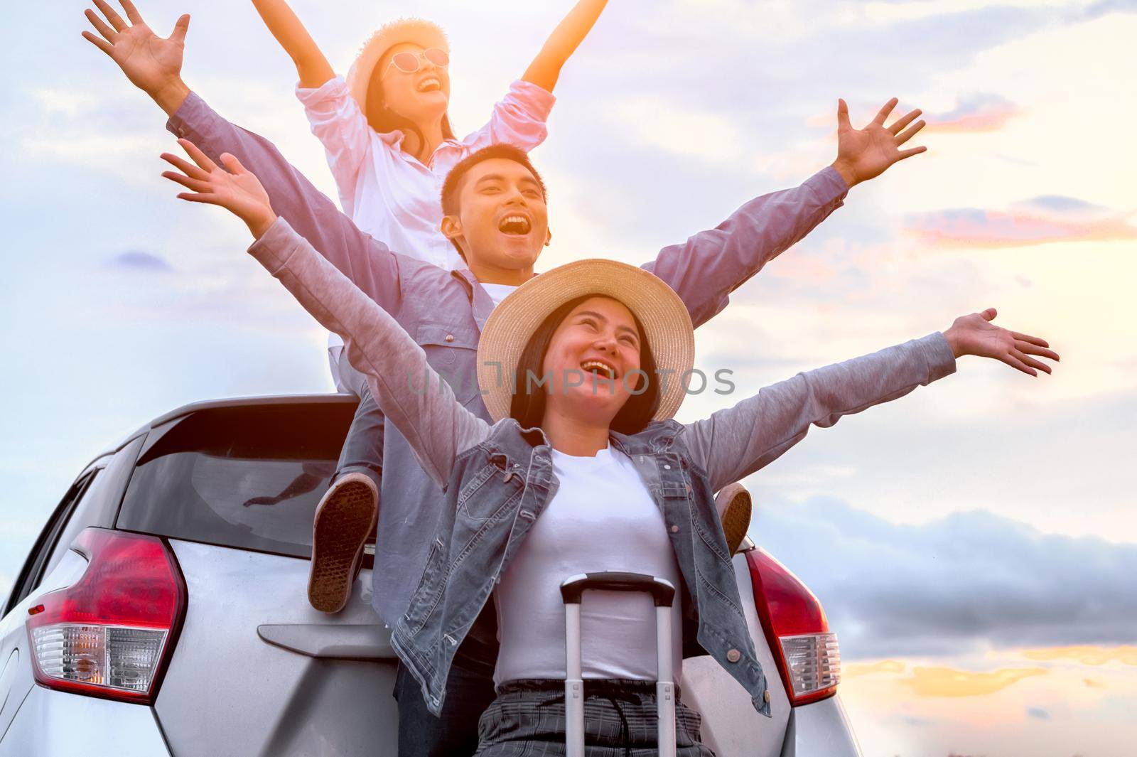 Happy Asian friends spread arms widely and breathed fresh air with happiness mood in on raod trip in car trunk. People lifestyle in long vacation trip concept. Outdoors nature and transportation