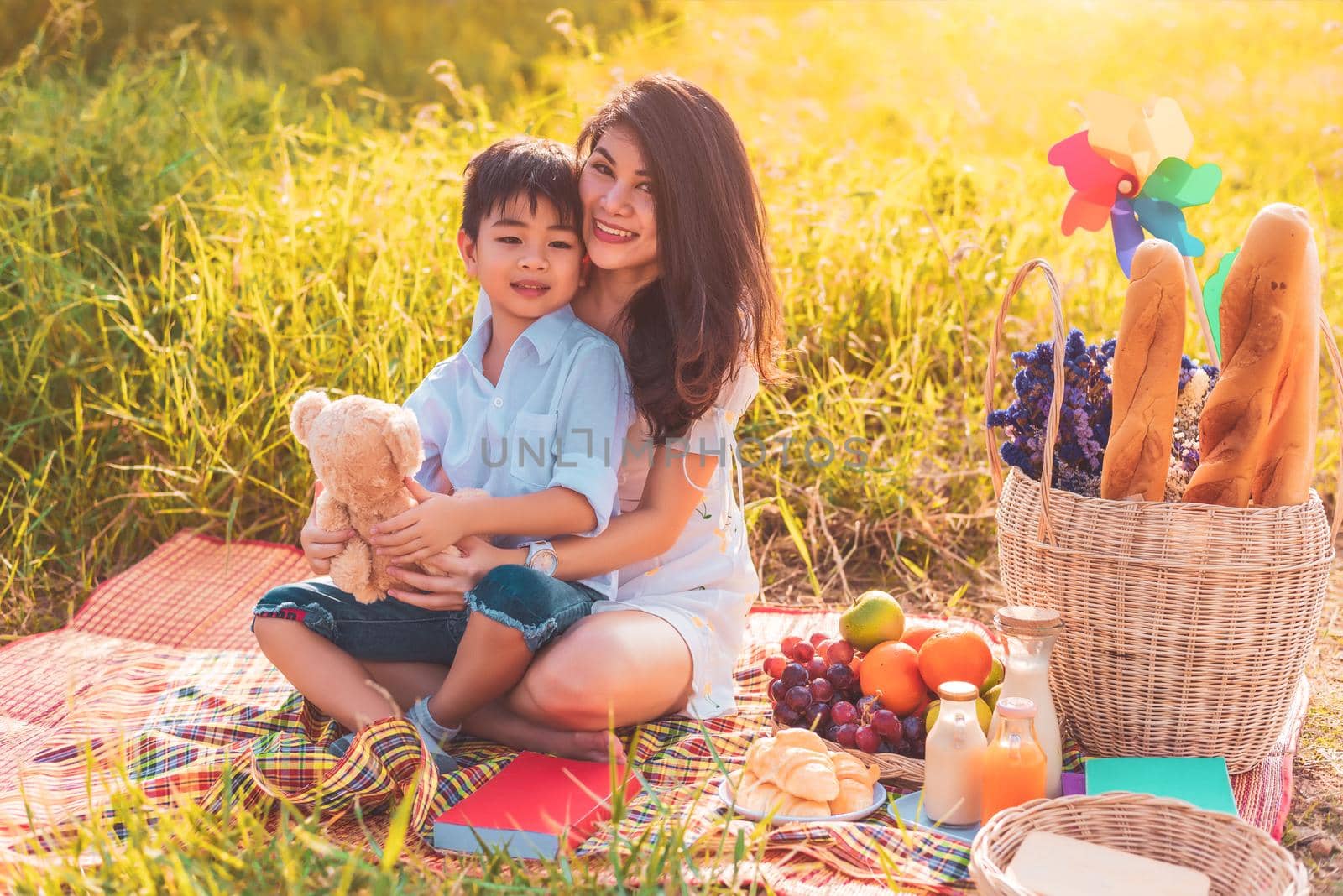 Beautiful Asian mother and son doing picnic and in Easter summer party on meadow near lake and mountain. Holiday and Vacation. People lifestyle and Happy family life concept. Thai person