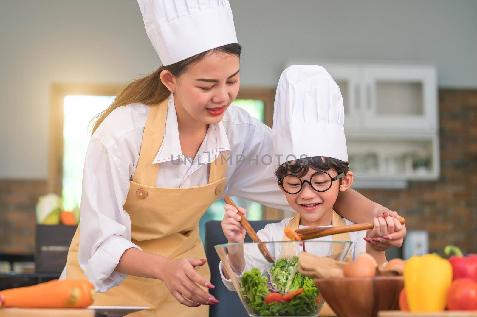 Happy beautiful Asian woman and cute little boy with eyeglasses prepare to cooking in kitchen at home. People lifestyles and Family. Homemade food and ingredients concept. Two Thai people life