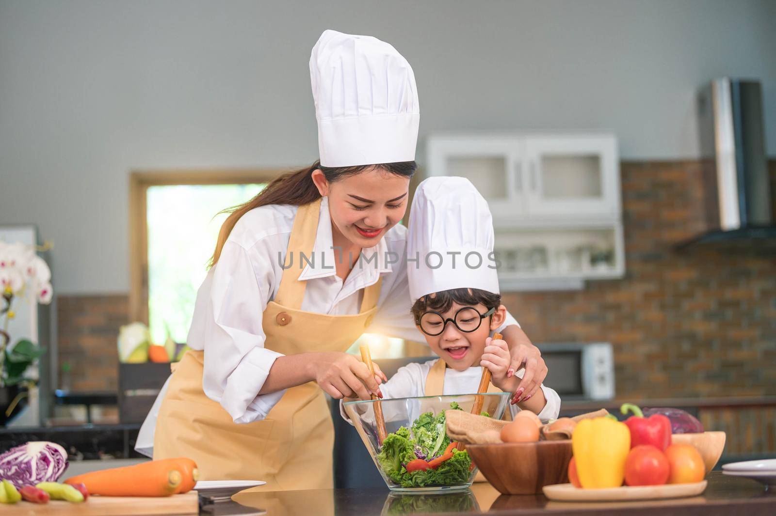 Happy beautiful Asian woman and cute little boy with eyeglasses prepare to cooking in kitchen at home. People lifestyles and Family. Homemade food and ingredients concept. Two Thai people life