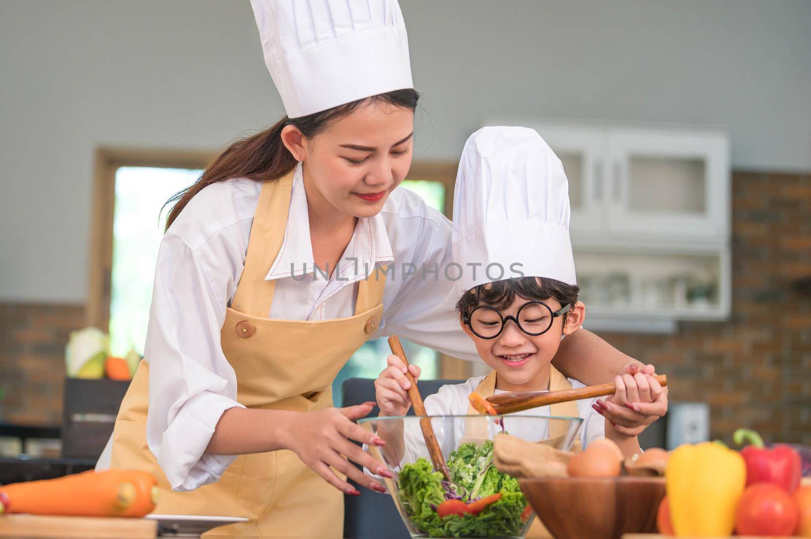 Happy beautiful Asian woman and cute little boy with eyeglasses prepare to cooking in kitchen at home. People lifestyles and Family. Homemade food and ingredients concept. Two Thai people life