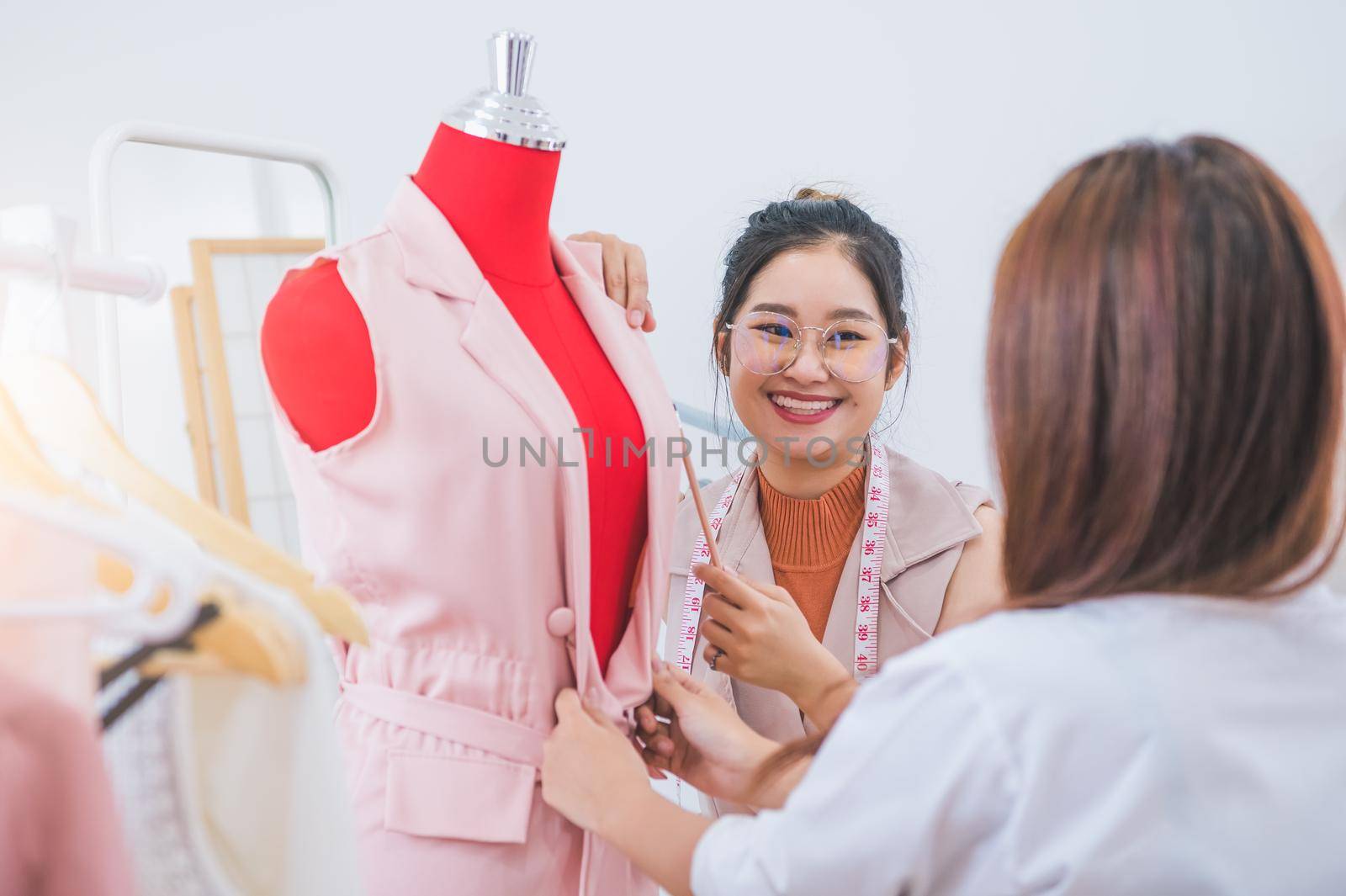 Attractive Asian female fashion designer working and recommending new design collection clothes on mannequin in clothing shop to customer. Tailor and sewing dressmaker. People lifestyle concept
