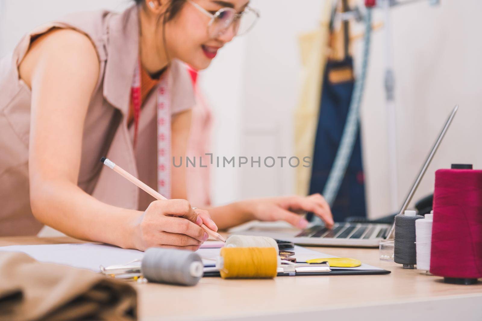 Attractive Asian female fashion designer working in home office workshop. Stylish fashionista woman creating new cloth design collection. Tailor and sewing. People lifestyle and occupation concept