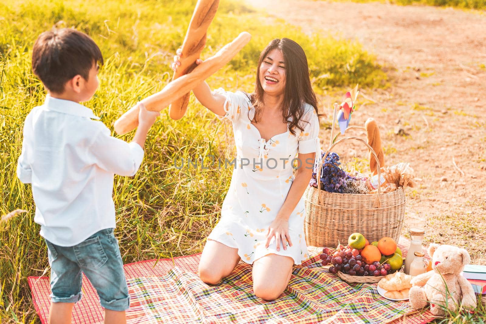 Mother and son play fencing with bread together when picnic at outdoors near lake or river. People lifestyles and Family. Motherhood and childhood concept. Spring and summer theme