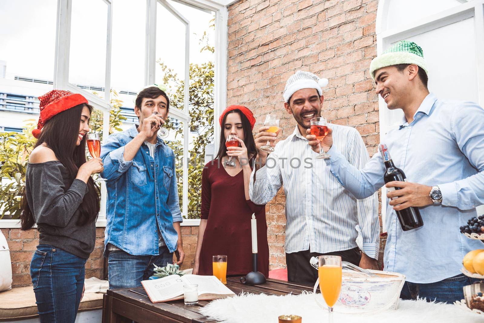 Outdoor Xmas party shot of young people toasting drinking glass at a rooftop terrace as forever friendship. Young friends hang out with alcohol drinking and juice. Christmas and New year party theme. by MiniStocker