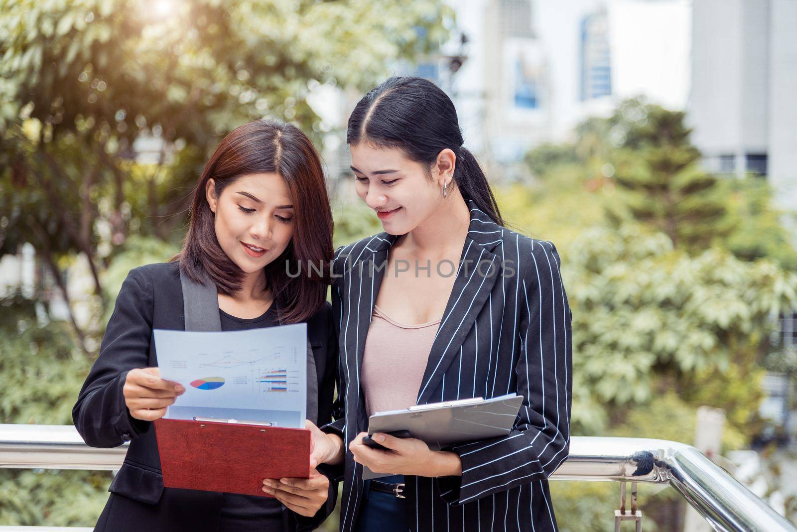 Two young Asian businesswomen looking into document file folder for analyzing profit or sale break even point after marketing. Business teamwork employees of lifestyle working women concept. by MiniStocker