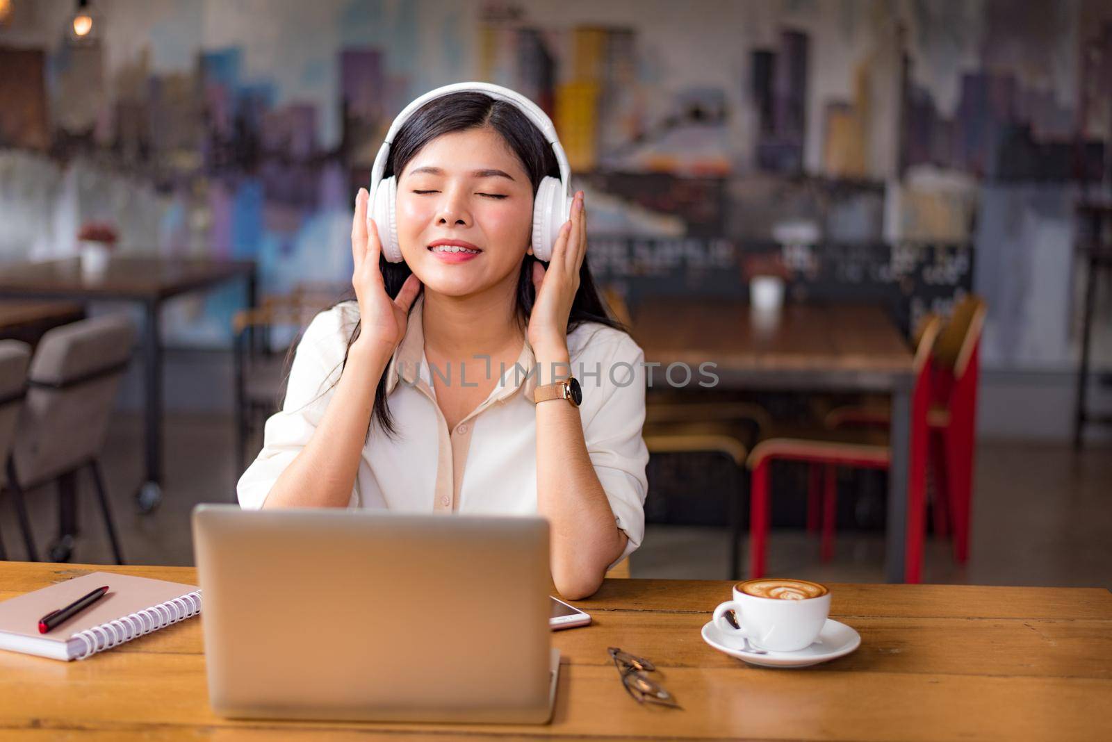 Beautiful Asian woman relaxing and listening to music in cafe with laptop computer and coffee cup. People and lifestyles concept. Freelance happy workplace theme. University and college theme.