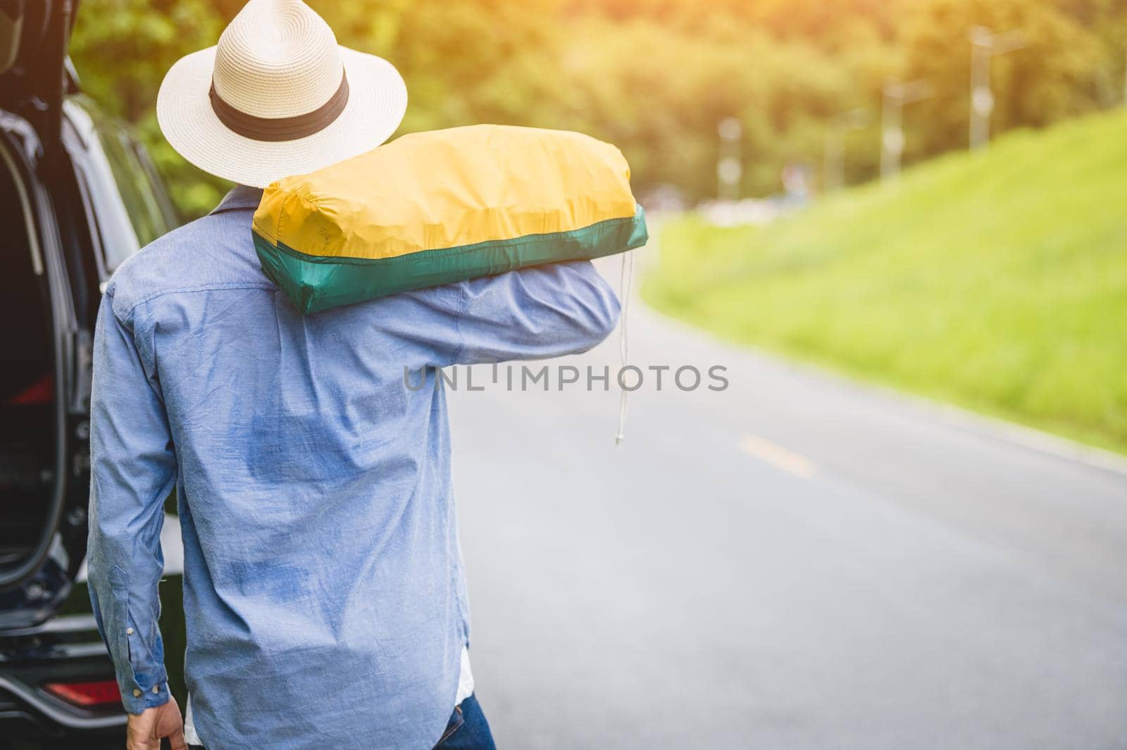 Back view of tourist walking along road with bag during travel in countryside. People lifestyles and vacation concept. Man holding and backpack for long holiday trip with mountain background