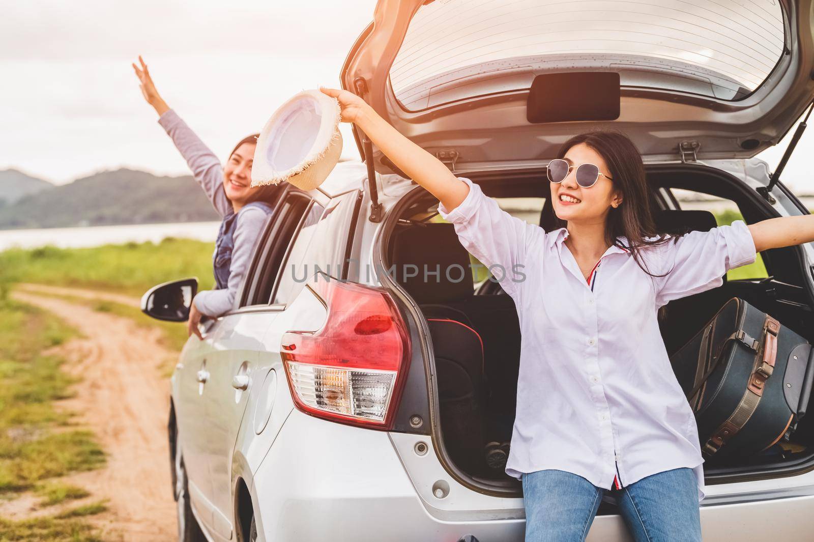 Happy Asian women friends spread arms out of window under sunset at seaside with nature  background during travel in holiday. Confidence cheerful girl with dawn sky. Sea and mountain. Vacation concept