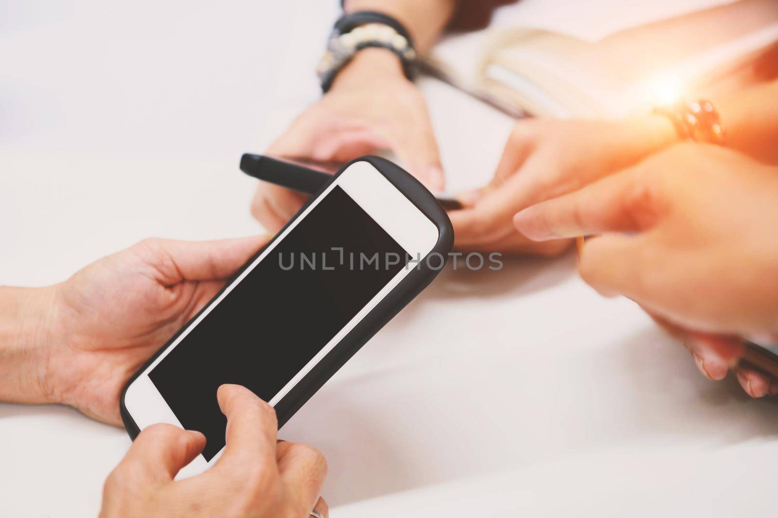 Multiracial friends hand using mobile addicted phone. Wifi connection people on meeting table. Teamwork concept with black blank touch screen phone. Charging and online share information theme.