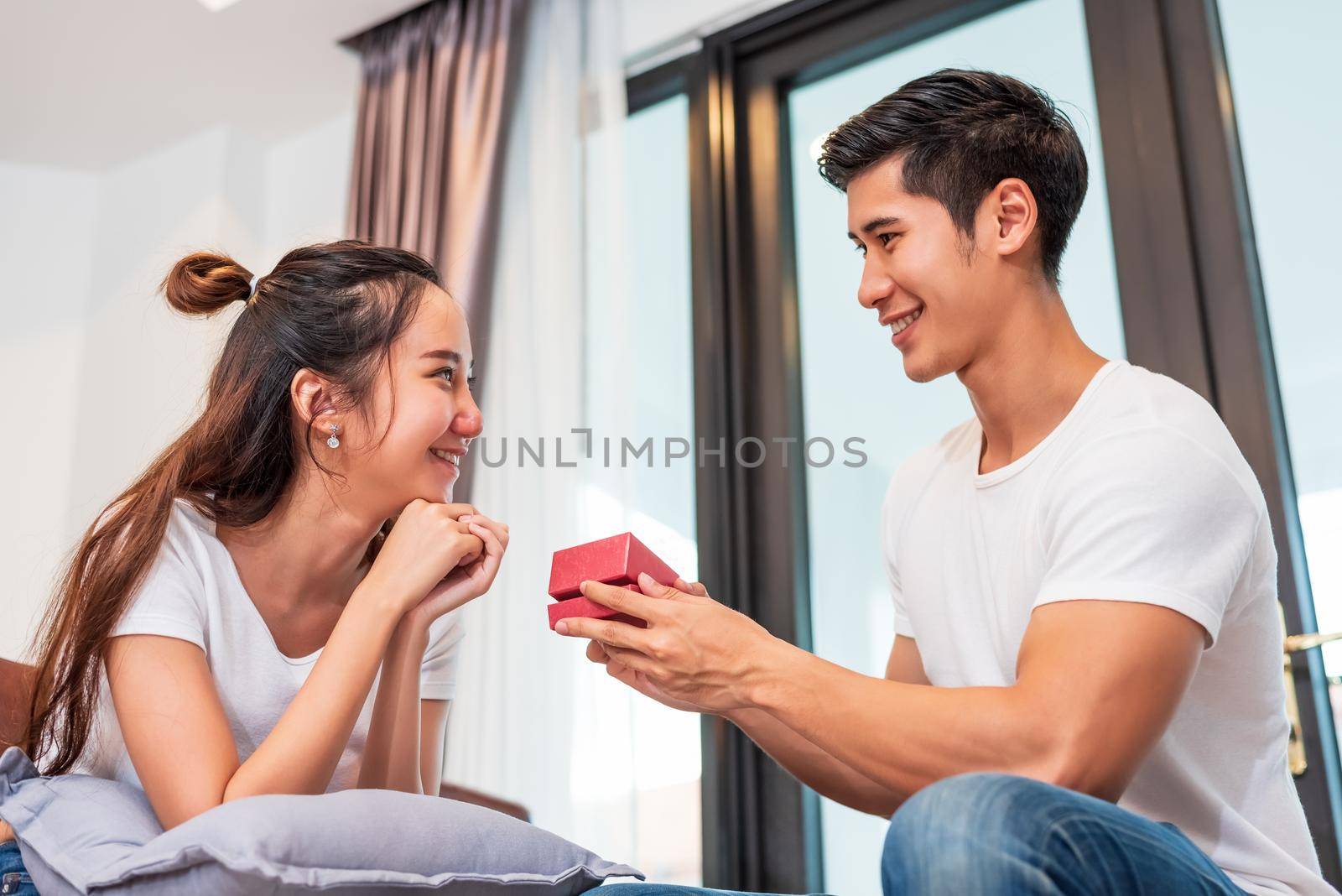 Man holding gift box for surprise girlfriend at their home. Woman waiting for Valentines gift form boyfriend. Happy Birthday party anniversary concept. People couple lifestyles and family life theme by MiniStocker