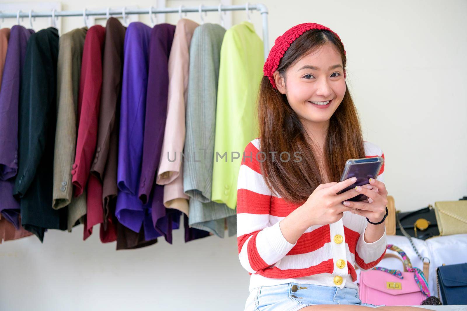 Beauty Asian Vlogger blogger selling woman clothes and bag online during using phone on social media. Woman coaching trading and review product. Business presentation. Looking at camera portrait by MiniStocker