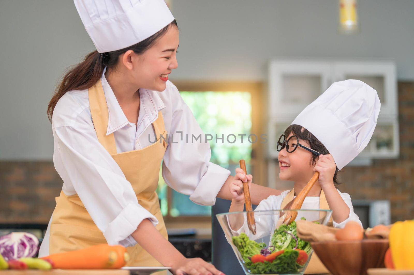 Happy beautiful Asian woman and cute little boy with eyeglasses prepare to cooking in kitchen at home. People lifestyles and Family. Homemade food and ingredients concept. Two Thai people life