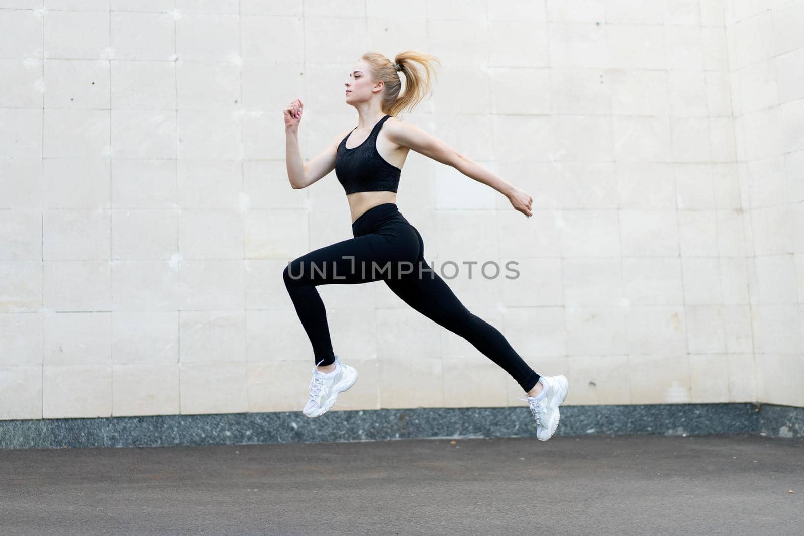 Sport and Fitness Concept Young Adult Caucasian Female Athlete Jumping High Outdoor Gray Tail Wall Background Sportive Woman Jump Exercises Outside Healthy Lifestyle Motivation