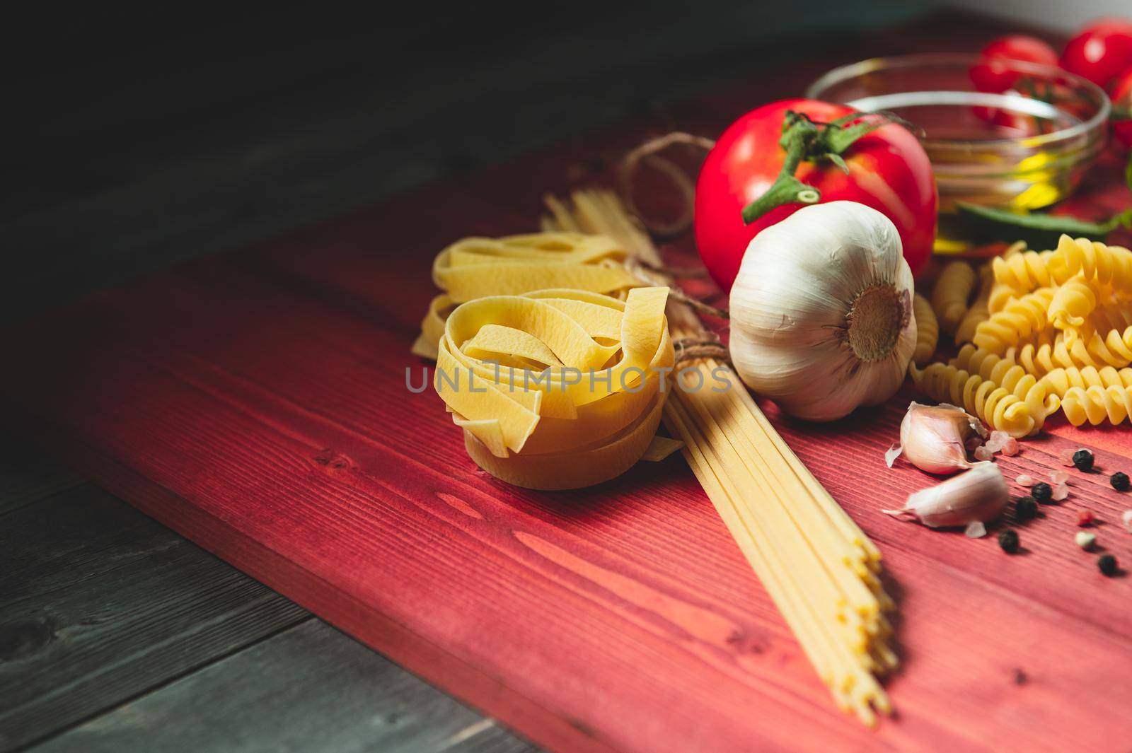 Tasty appetizing italian spaghetti pasta ingredients for kitchen cuisine with tomato, cheese parmesan, olive oil, fettuccine and basil on wooden brown table. Food Italian recipe homemade. Top view